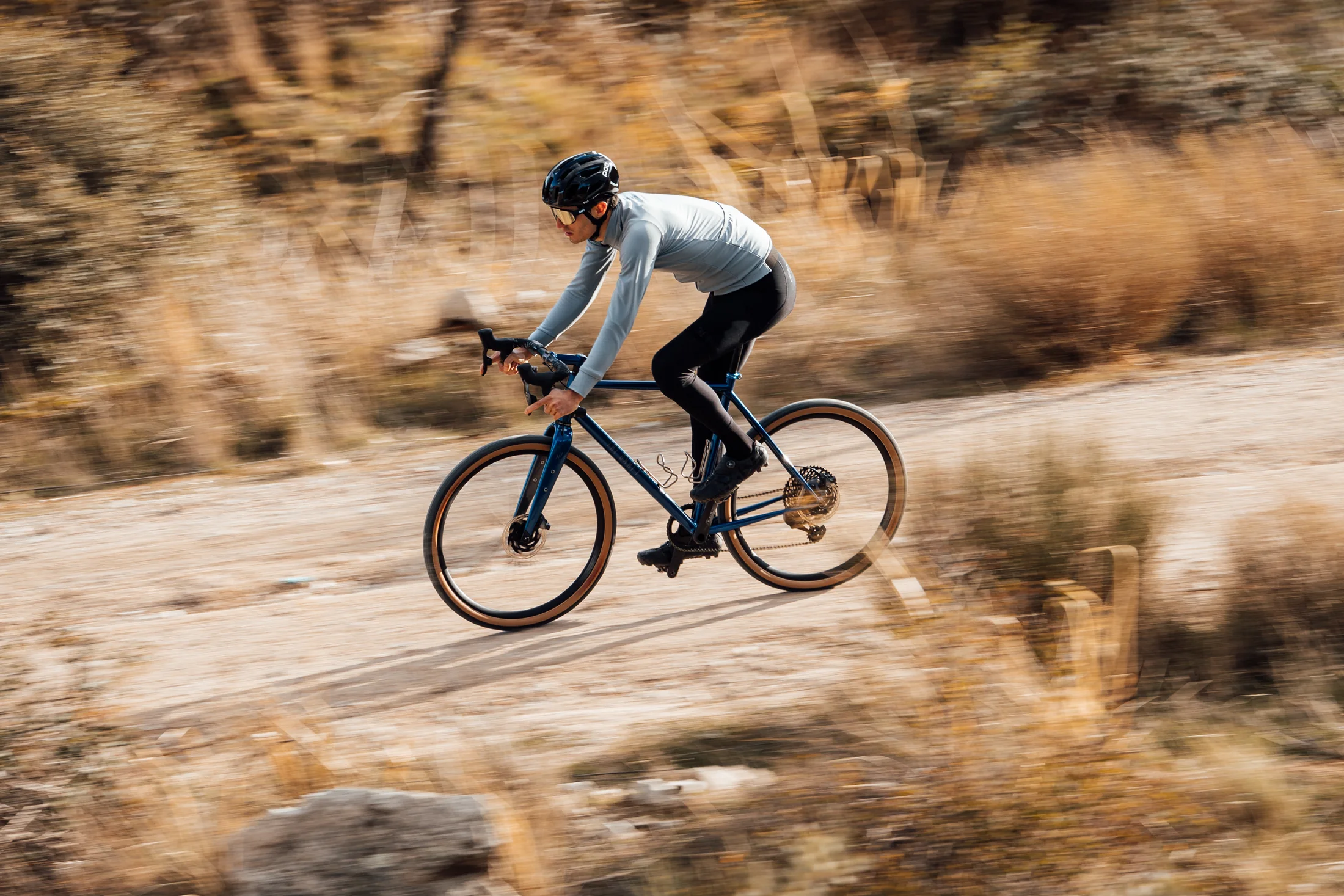 A cyclist riding a blue The Draft bicycle on a gravel track.